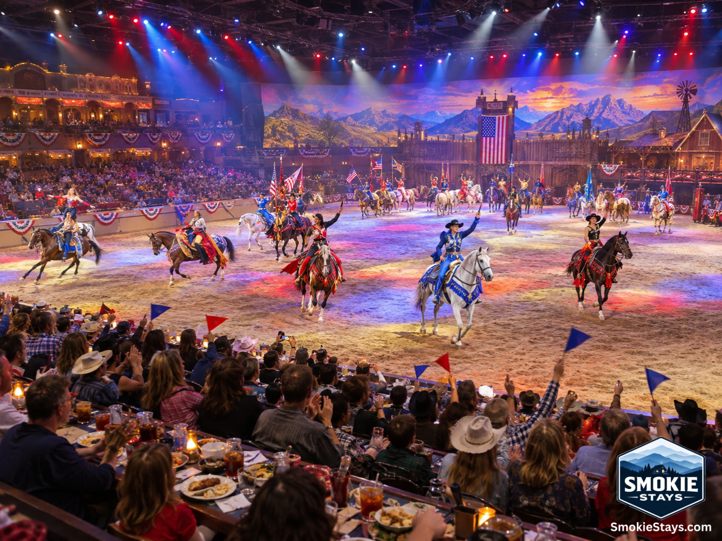 Horses and riders in colorful costumes perform choreographed stunts in a massive dinner show arena in Pigeon Forge, Tennessee, with a packed audience at dining tables cheering and waving pennants in the foreground.